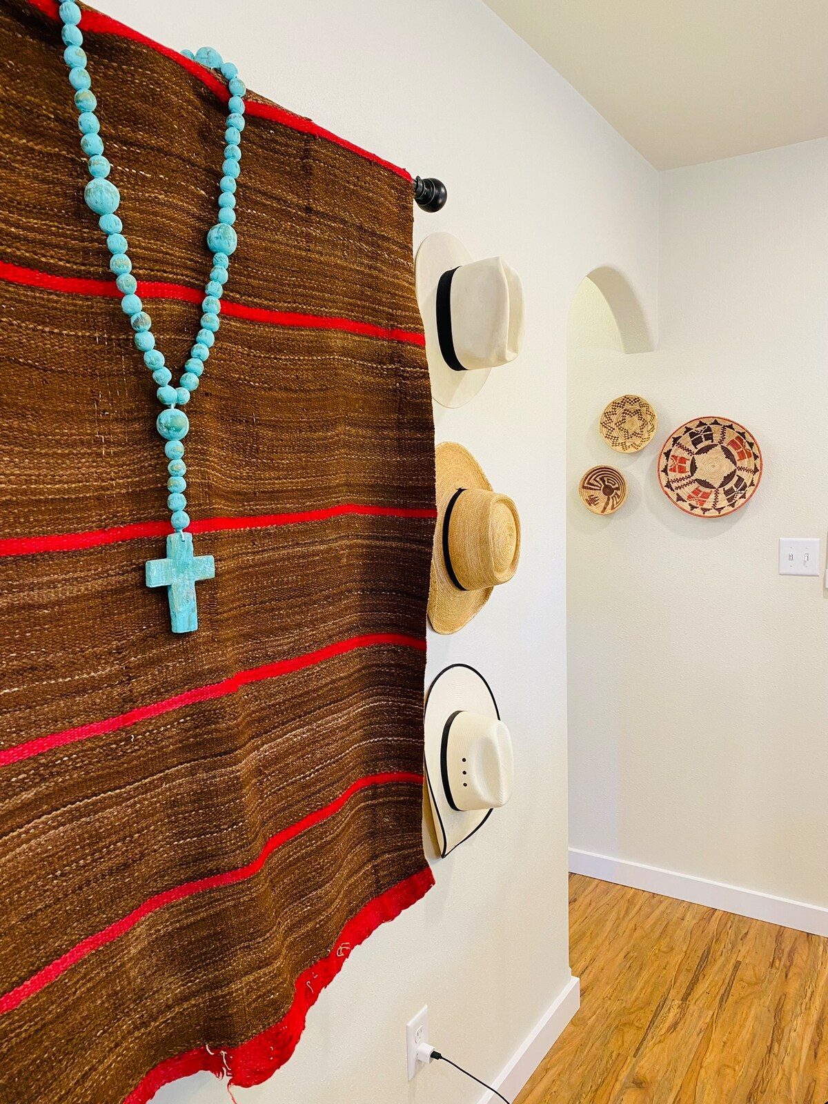 Woven wall hanging with a turquoise cross and straw hats