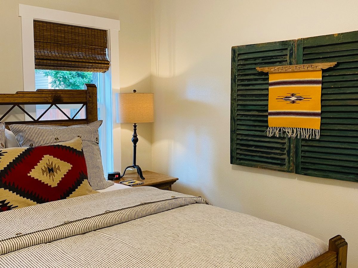 Bedroom with wood bed and a green shutter hung with a woven textile
