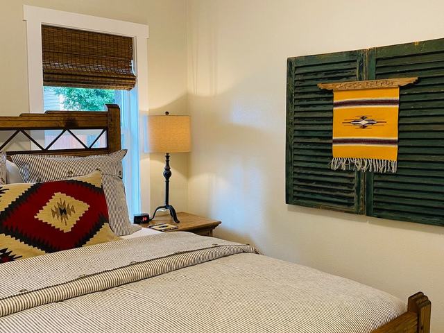 Bedroom with wood bed and a green shutter hung with a woven textile